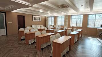 A conference room with multiple tables and chairs, large windows, and a wooden floor.