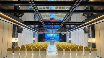 A conference room with rows of chairs, a stage at the front, and a large screen.