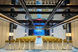Sala de conferências com fileiras de cadeiras, um palco na frente e uma tela grande.