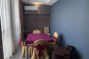 A room with a table set for four, a chair with a red bow, a small wooden table, and a wall-mounted air conditioner. - Gangxing Hotel (Zhuji)