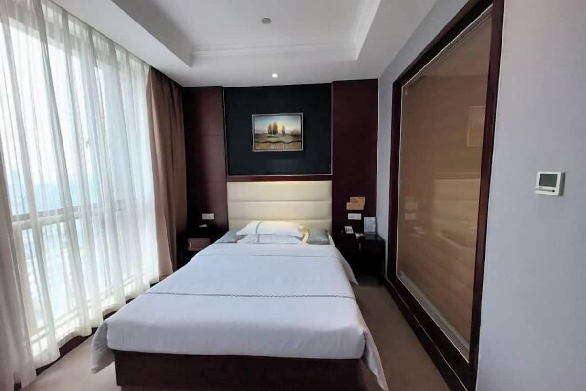 A hotel room with a large bed, a headboard, a nightstand, a wall-mounted TV, and a large window with curtains.