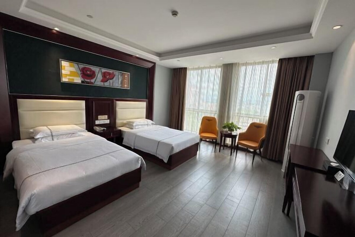A hotel room with two beds, a TV, a desk, a chair, and a window with curtains.