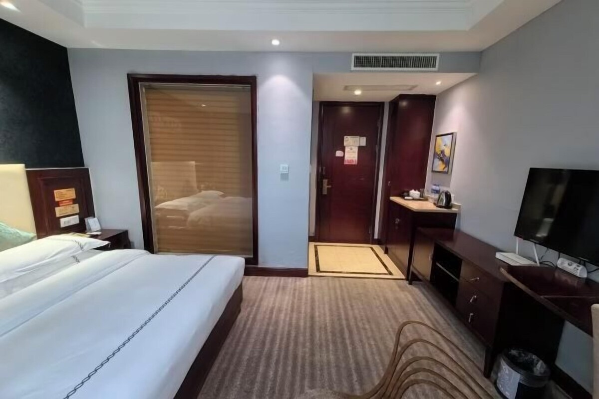A hotel room with a bed, a desk with a computer, a television, and a door leading to a bathroom.