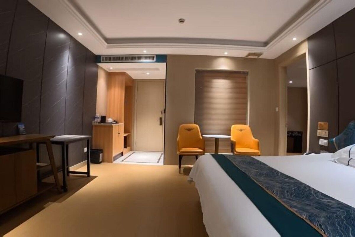 A hotel room with a bed, a desk, two chairs, a television, and a wardrobe.