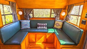 A cozy interior with a built-in bench seating area, wooden flooring, and large windows with curtains.