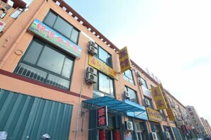 A multi-story building with various commercial establishments on the ground floor, including a restaurant and a shop with a yellow sign. - Qingdao Dexinsheng Hotel (Qingdao)