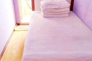 A bed with a white mattress and pillows, a wooden floor, and a door leading to a bright area. - Qingdao Dexinsheng Hotel (Qingdao)