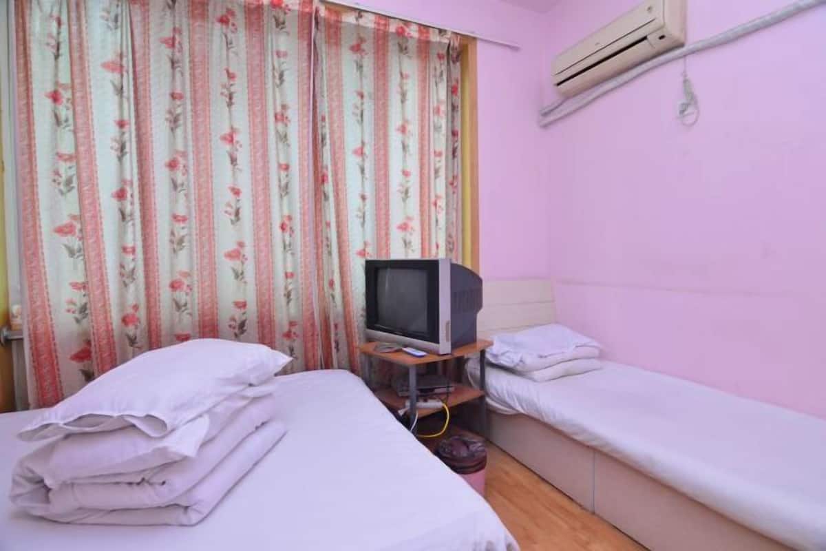 Een kleine kamer met twee bedden, een televisie op een standaard en een airconditioning aan de muur.