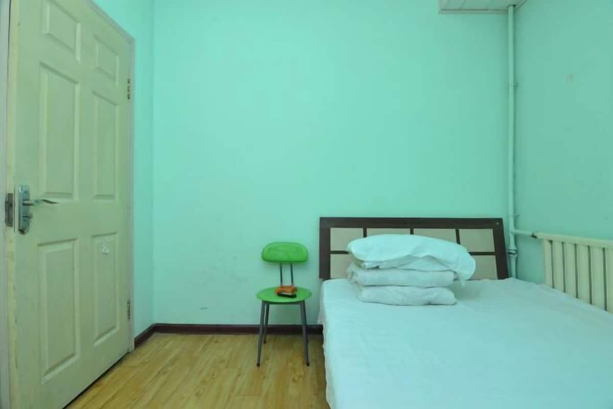 Een kleine, schone kamer met een enkel bed, een stoel en een deur.
