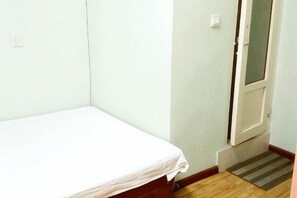 A single bed in a room with a door and a wooden floor. - Qingdao Dexinsheng Hotel (Qingdao)