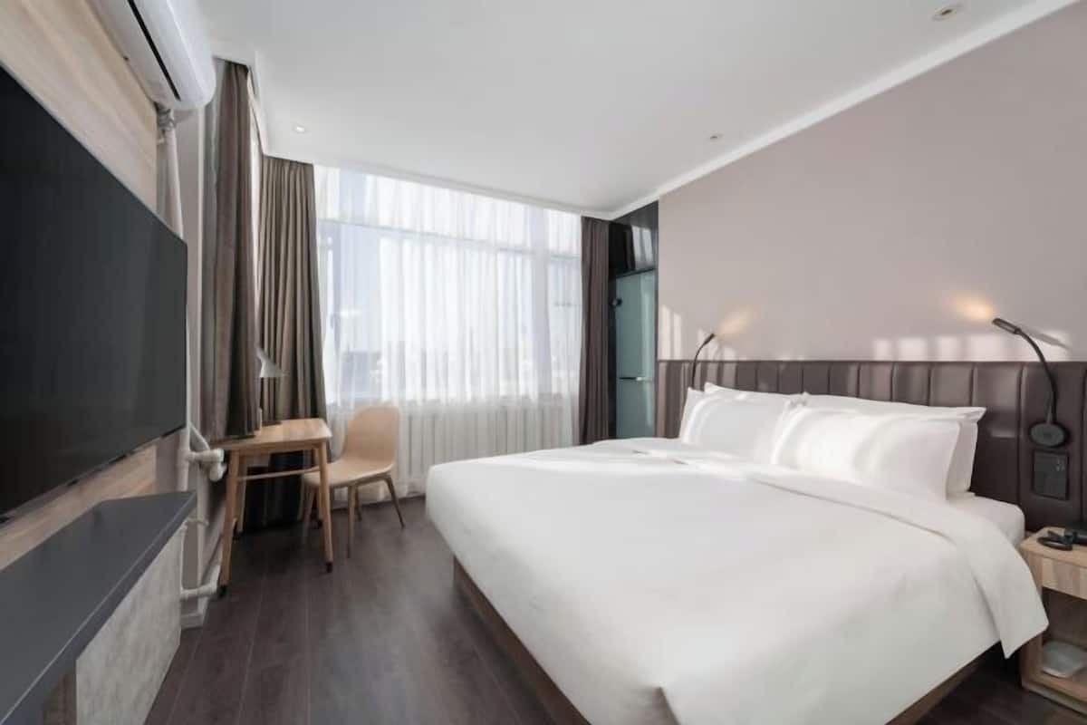 A hotel room with a bed, a desk, a chair, a TV, and a window with curtains.
