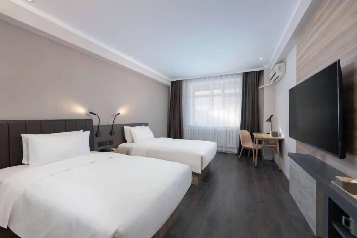 A hotel room with two beds, a desk, a chair, a television, and a window with curtains.
