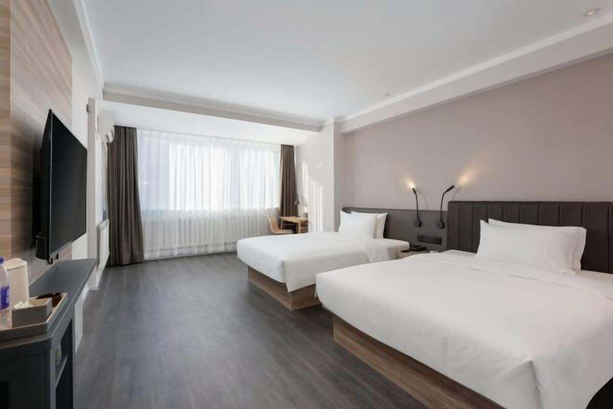 A hotel room with two beds, a TV, a desk, and a window with curtains.