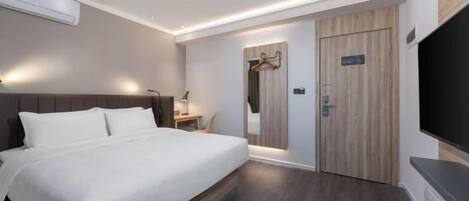 A modern hotel room with a large bed, a desk with a lamp, a mirror, and a TV mounted on the wall.