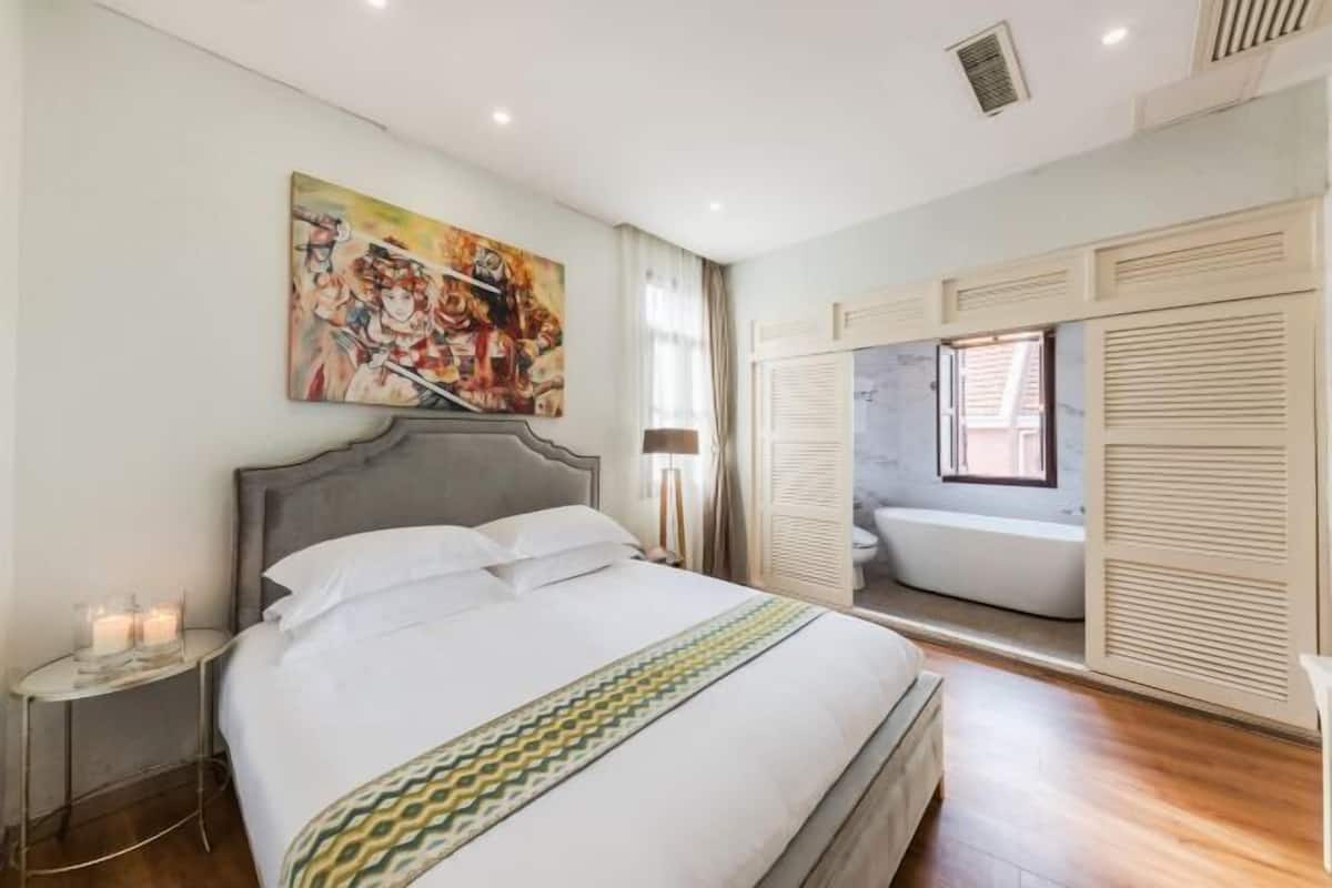 Ένα υπνοδωμάτιο με ένα κρεβάτι, ένα κομοδίνο, διακοσμητικά στον τοίχο και ένα μπάνιο με μπανιέρα.