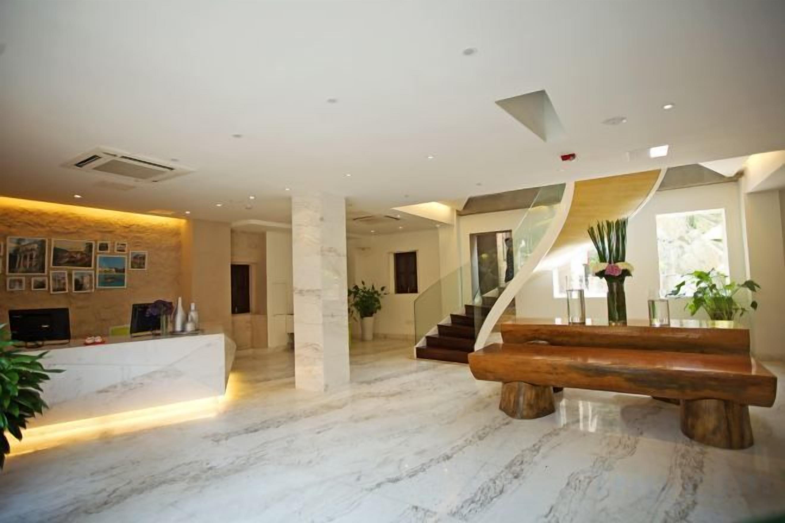 A spacious lobby with a marble floor, a reception desk, a staircase, and a large wooden bench.