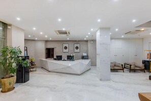 Un hall d’hôtel avec un sol en marbre, un comptoir d’accueil, un espace salon et une grande plante en pot.