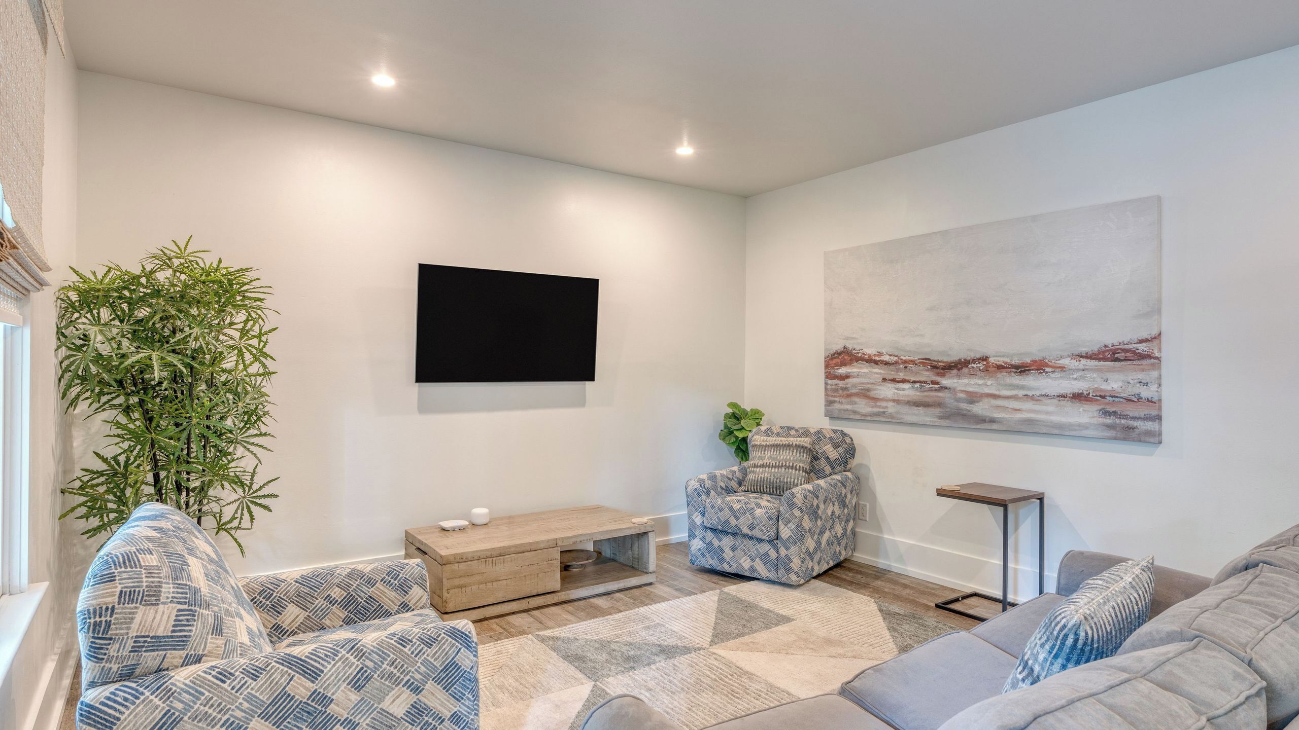 Un salon moderne avec un téléviseur à écran plat, un tableau, une grande plante et des meubles à motifs.