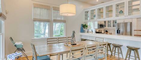 Una cocina moderna con armarios blancos, una isla central y un comedor con sillas y una mesa de madera.