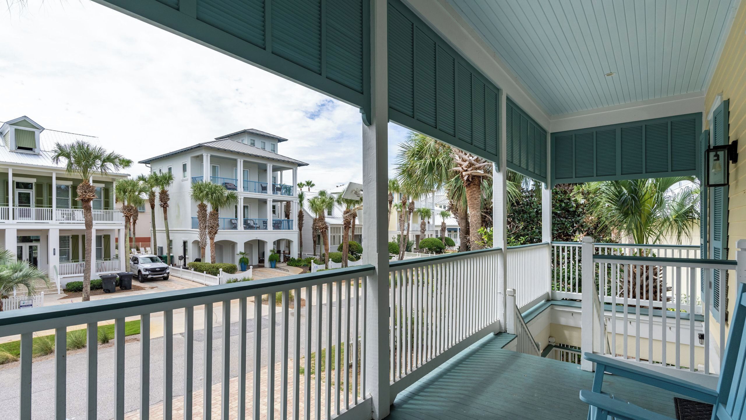 A covered balcony with a railing, overlooking a street with multi-story buildings and palm trees.