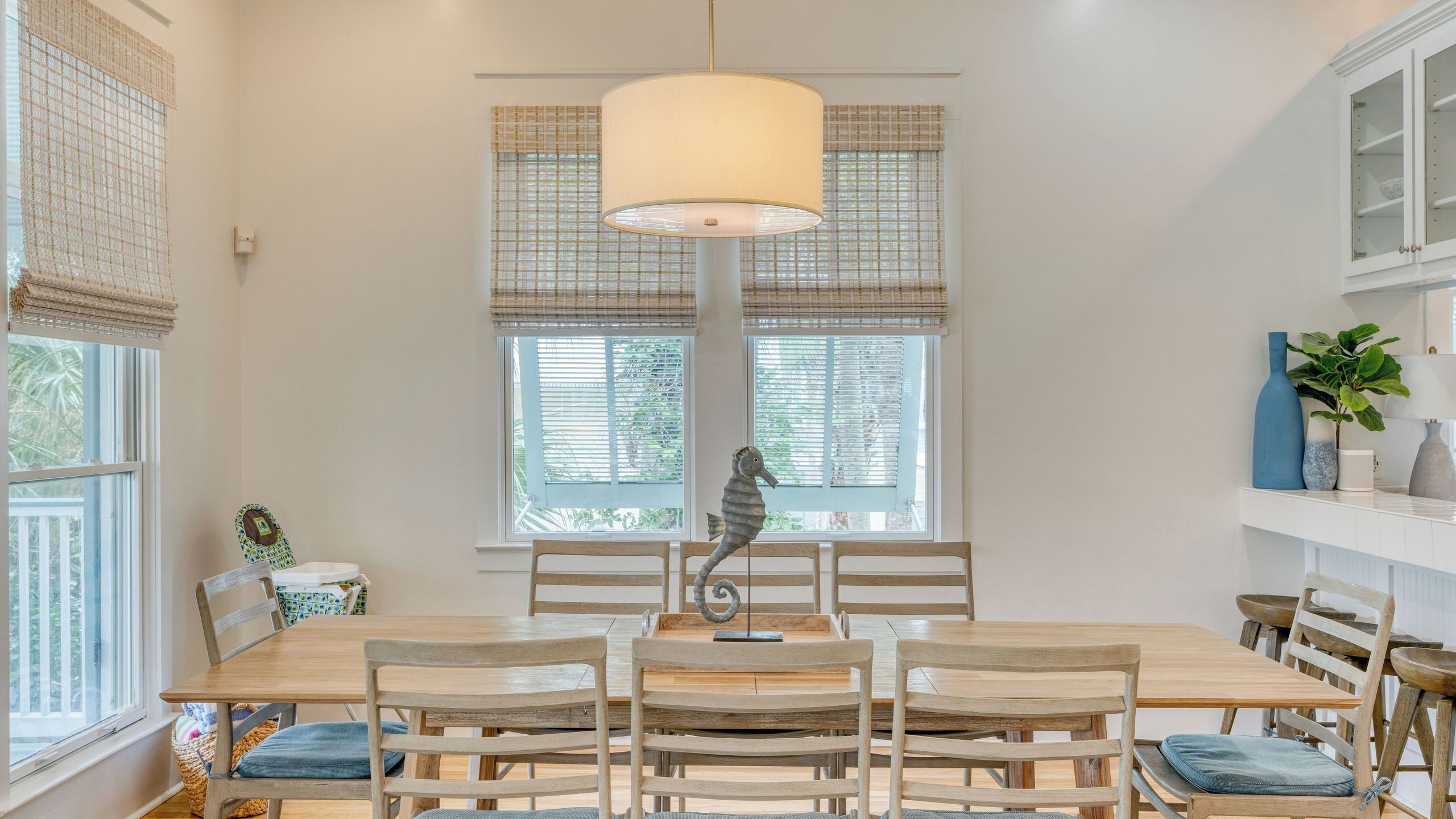 A dining area with a wooden table, chairs, a hanging lamp, and a decorative seahorse.