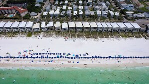 An aerial view of a beach with a row of beach houses and a sandy beach with umbrellas and people. - Destin Dream by Avantstay 2-story Home, Walk to Beach (Miramar Beach)