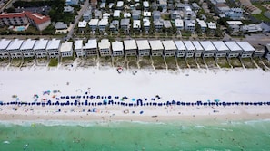 An aerial view of a beach with a row of beach houses and a sandy beach with umbrellas and people. - Destin Dream by Avantstay 2-story Home, Walk to Beach (Miramar Beach)