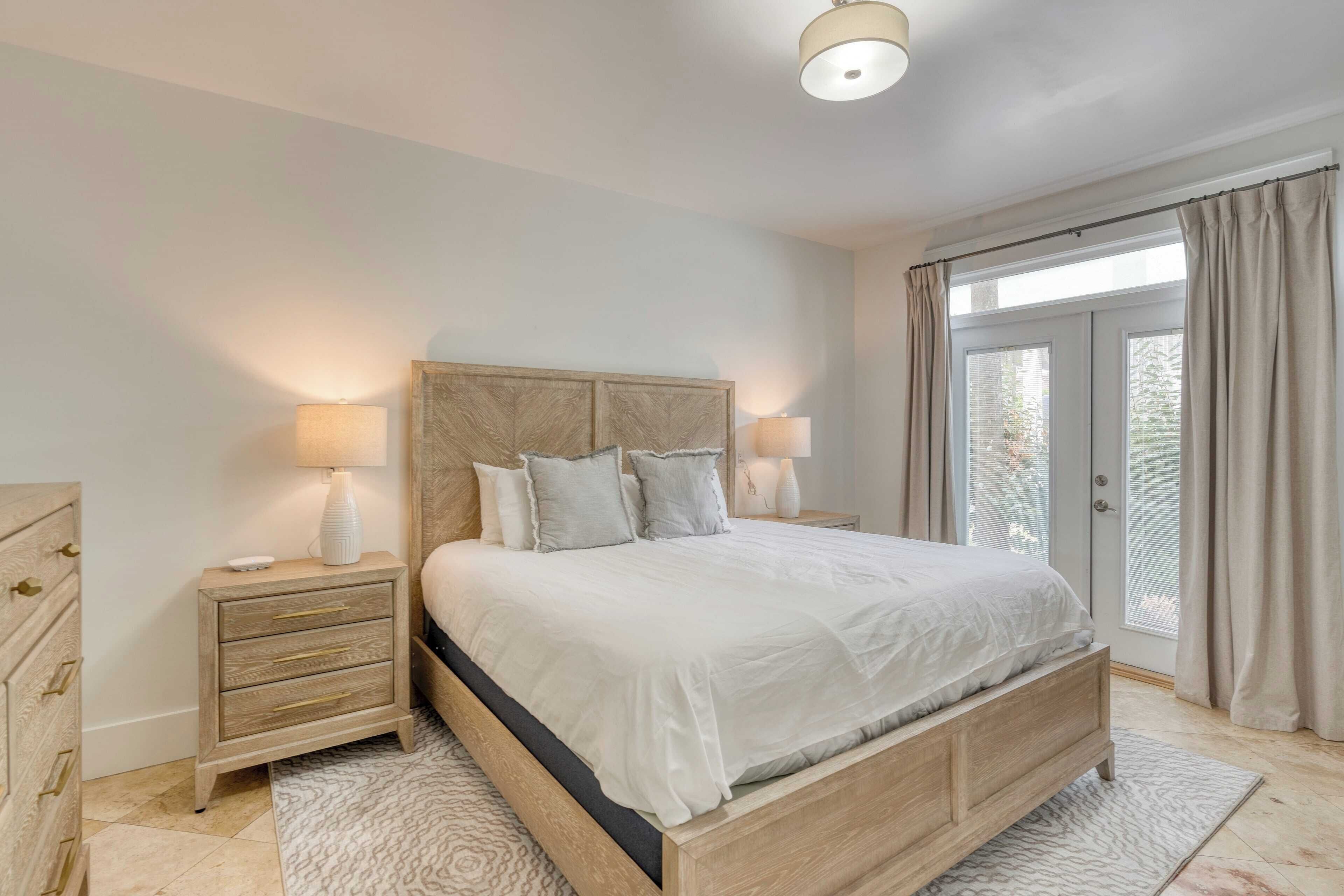 Un dormitorio con cama, mesitas de noche, cómoda y un amplio ventanal con cortinas.
