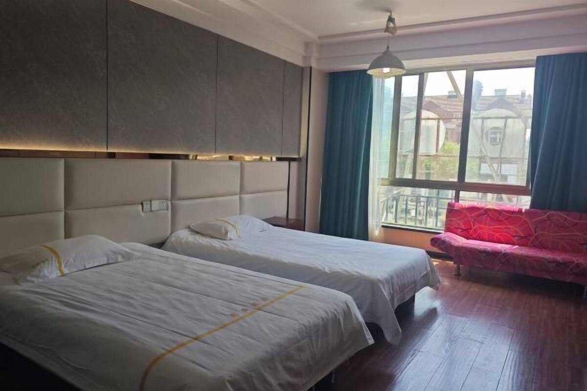 A hotel room with two beds, a sofa, a large window, and a view of buildings outside.