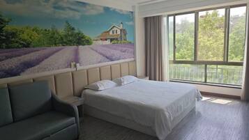 A bedroom with a bed, a nightstand, a sofa, a large window with a view of trees, and a mural of a house and field.