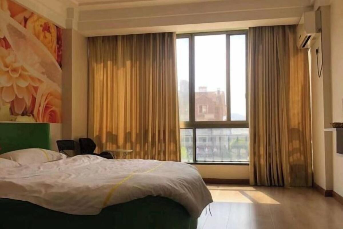 A hotel room with a large bed, a view of the city through a window, and a painting on the wall.