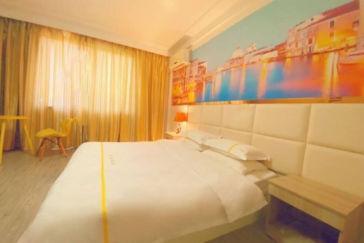 A hotel room with a large bed, a headboard, a nightstand, a lamp, a chair, and a painting of a cityscape.