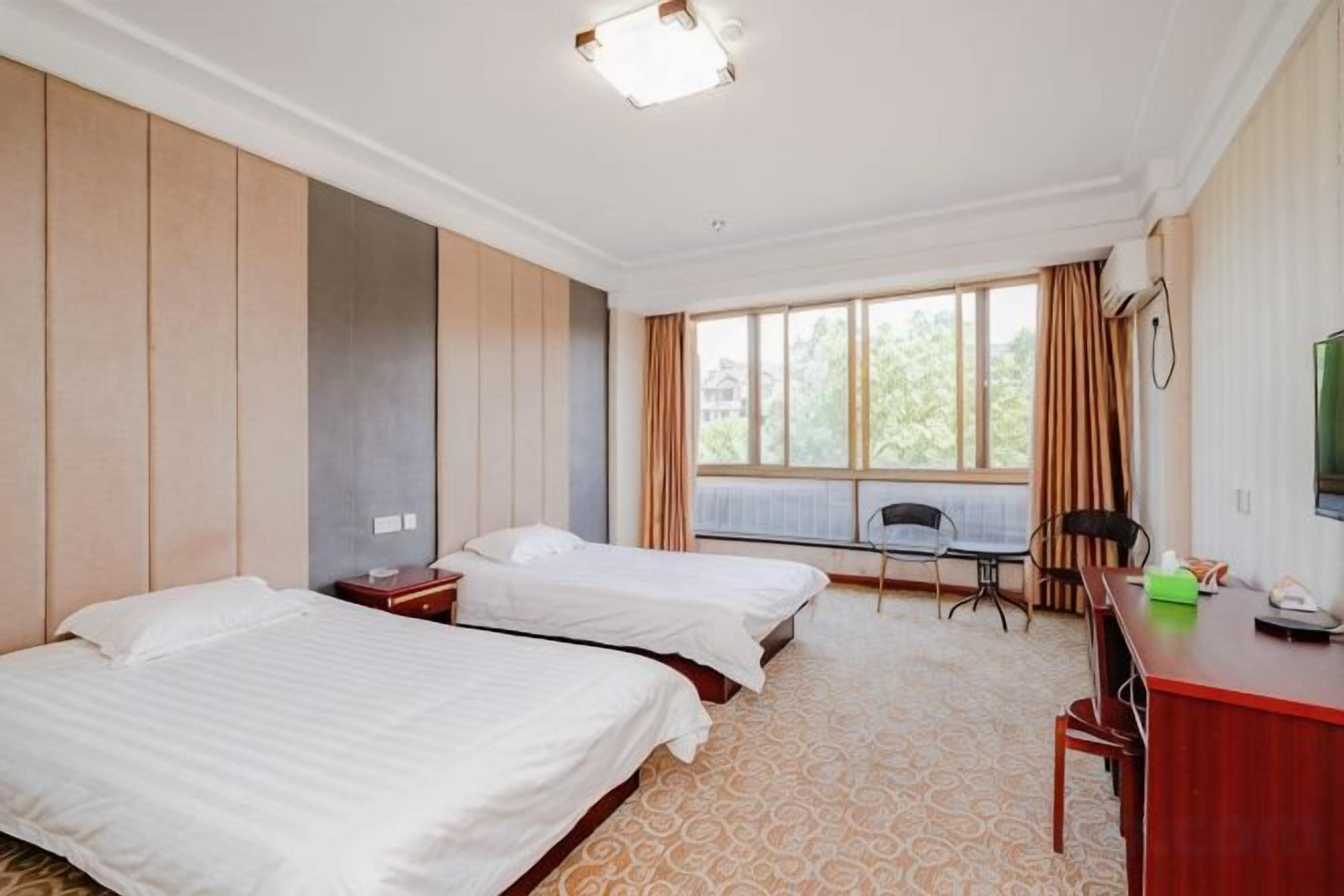 A hotel room with two beds, a desk, a chair, and a large window.