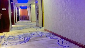 Un couloir d’hôtel avec un tapis à motifs et un plafond éclairé de lumières bleues.