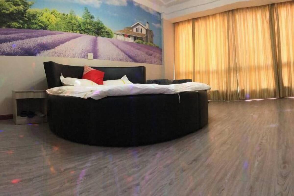 A round bed in a room with a mural of a lavender field and a house.