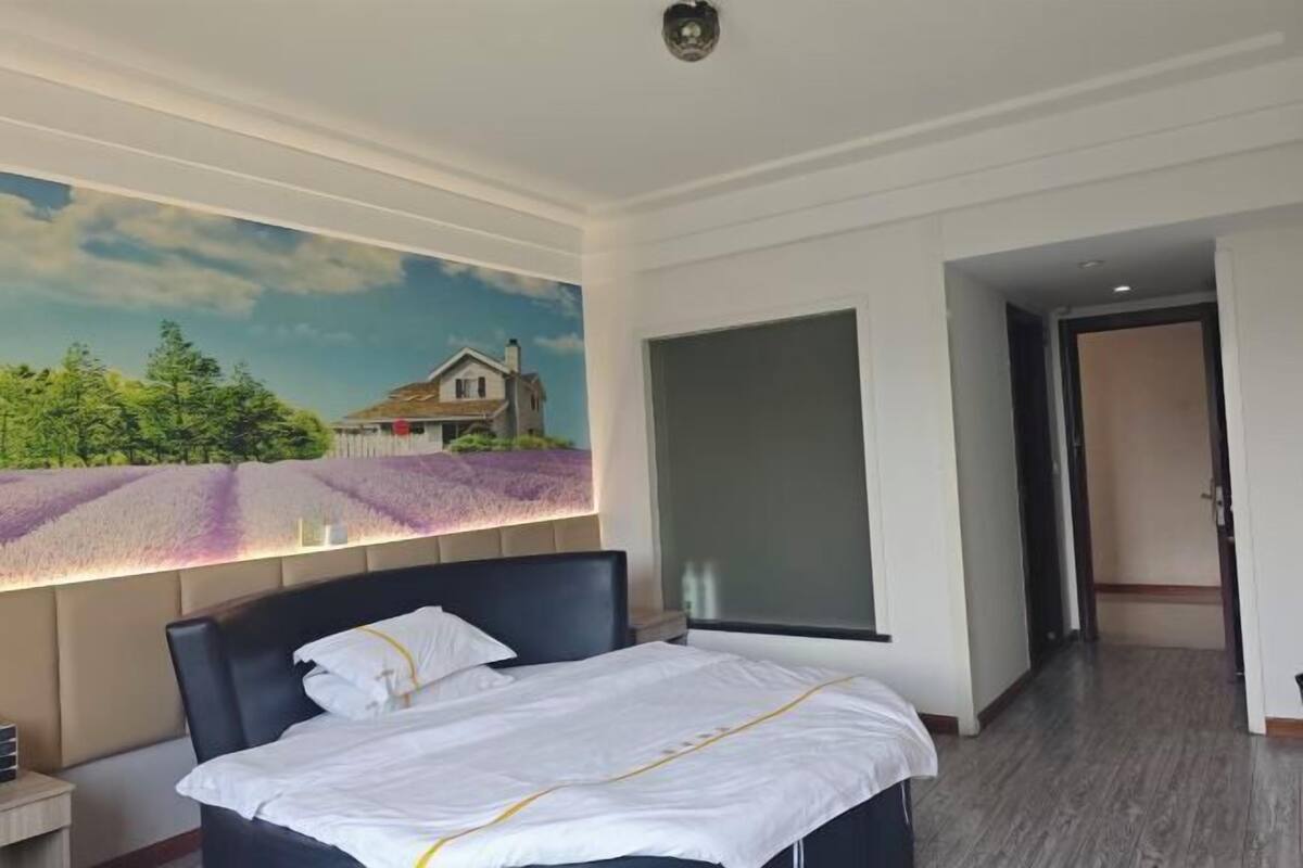 A hotel room with a bed, a nightstand, a wall-mounted TV, and a large window.
