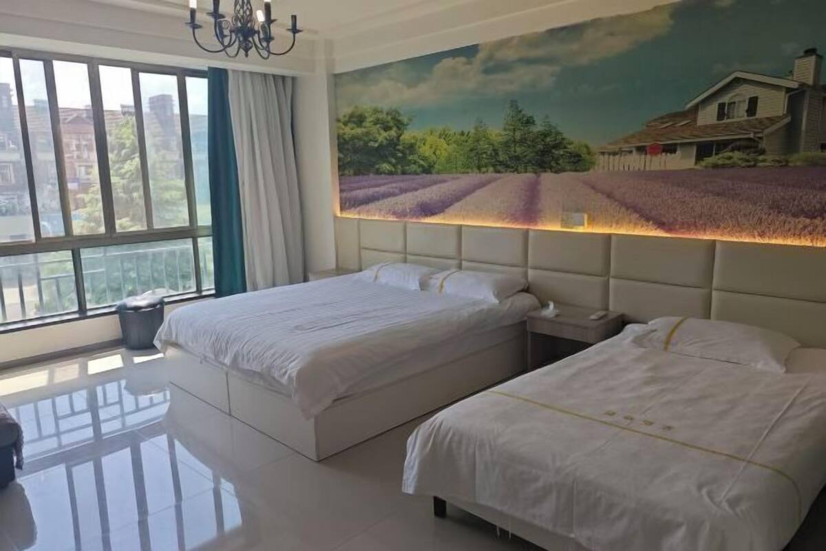 A hotel room with two beds, a large window, a chandelier, and a mural of a field.