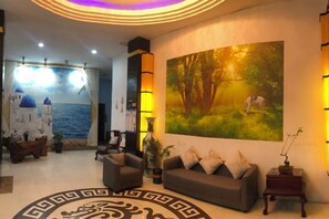 A lobby with a sofa, a coffee table, a painting of a tree, and a mural of a coastal scene. - Blue Sen Hotel (Tiantai Mountain Scenic Area) (Tiantai County)
