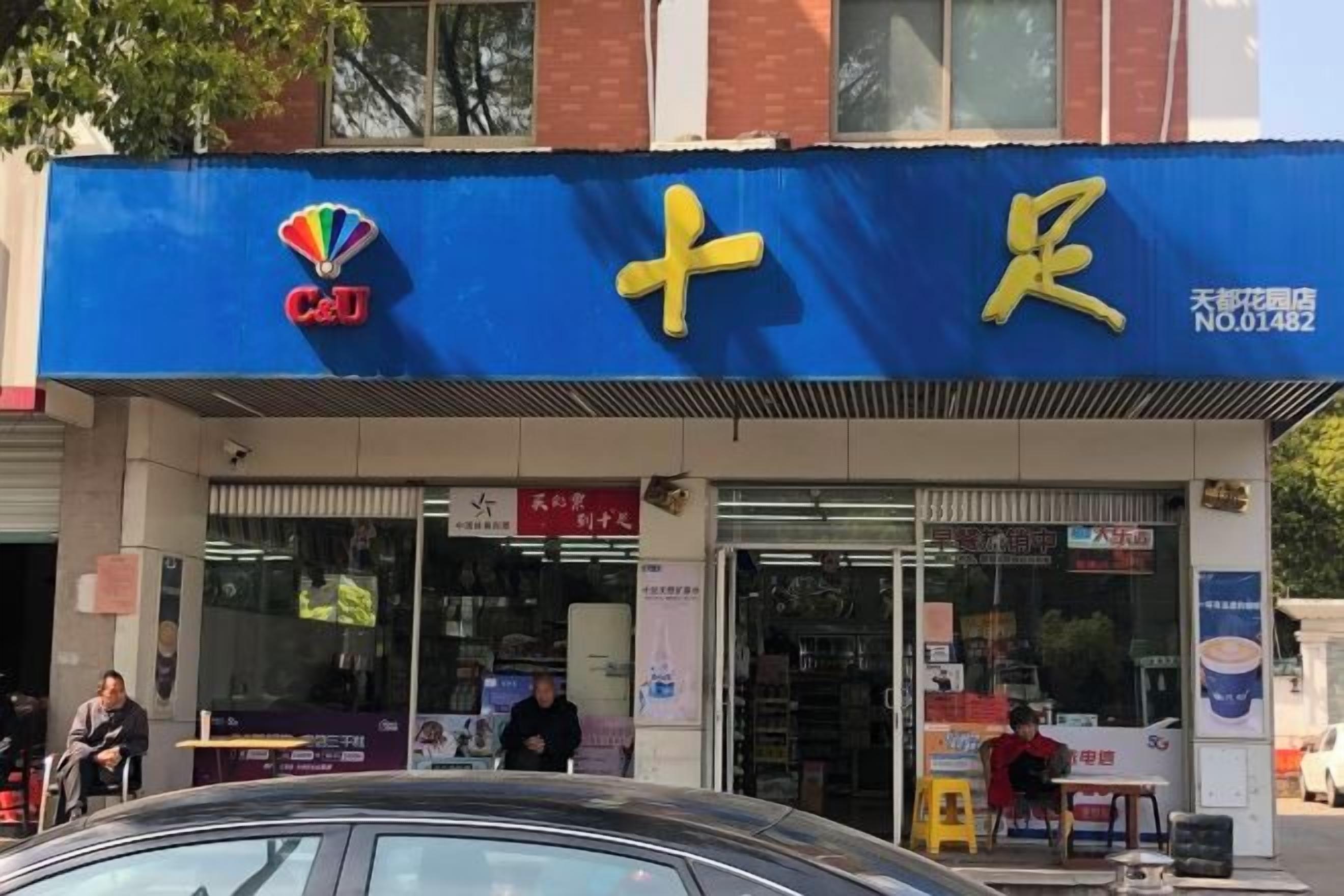 Un escaparate con toldo azul, un logotipo visible y un cartel con caracteres chinos.