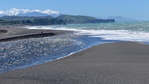 Une plage bordée d’une côte rocheuse, d’une barrière en béton et d’une chaîne de montagnes lointaine.