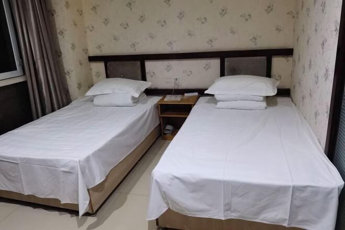 A room with two single beds, each with a wooden headboard and white bedding.