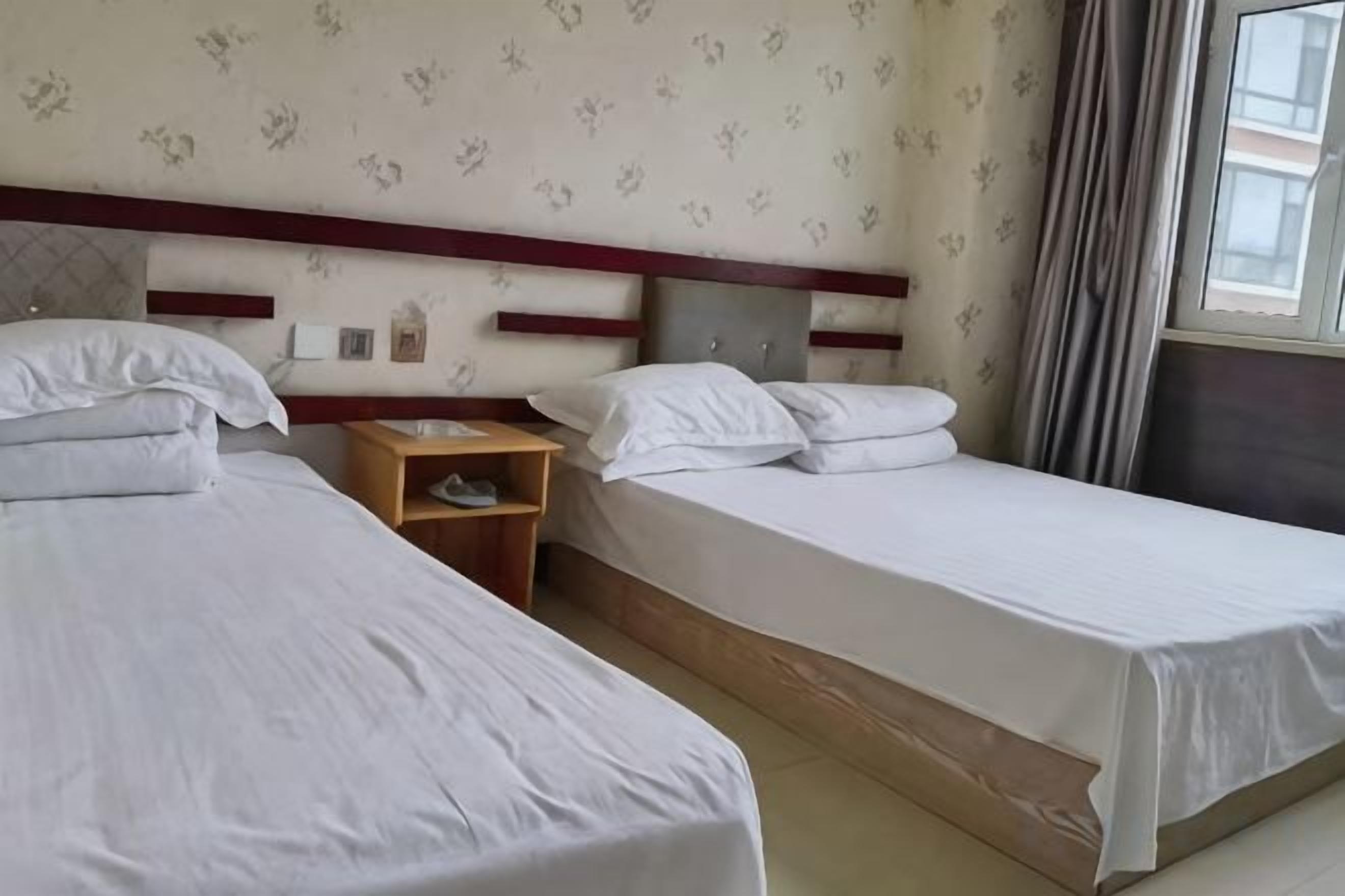 A hotel room with two single beds, a wooden nightstand, and a window with curtains.