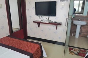 A hotel room with a bed, a television mounted on the wall, a small table, and a bathroom visible through a glass door. - Baihequan Hotel (Antu)