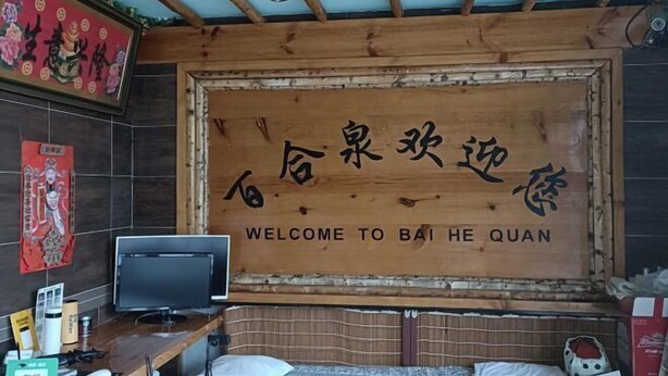 Une pièce dont un mur en bois est orné de caractères chinois et d’un texte en anglais, accueillant les visiteurs à Bai He Quan.