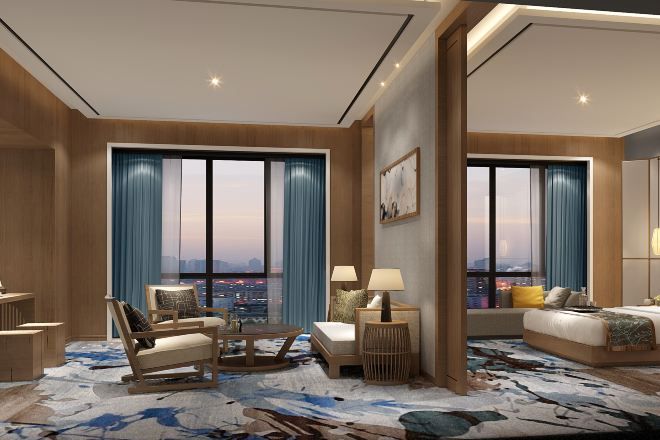 A modern hotel room with a large bed, a seating area with a coffee table, and a view of the cityscape through large windows.