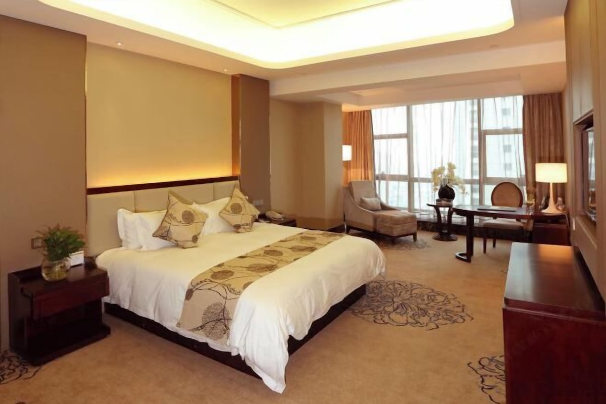 A hotel room with a large bed, a desk, a chair, and a window with curtains.
