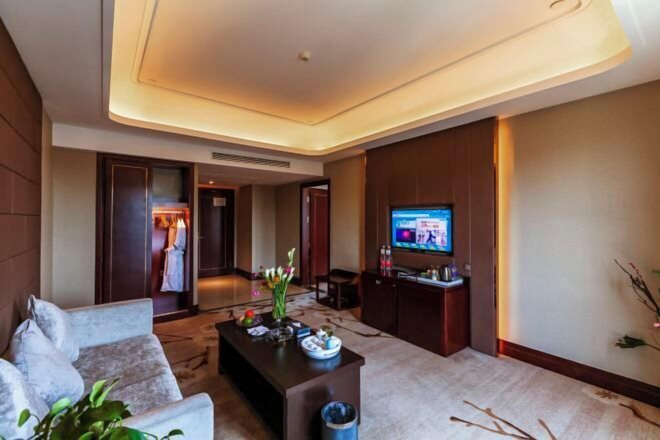 A modern hotel room with a sofa, a coffee table, a TV, and a decorative vase.