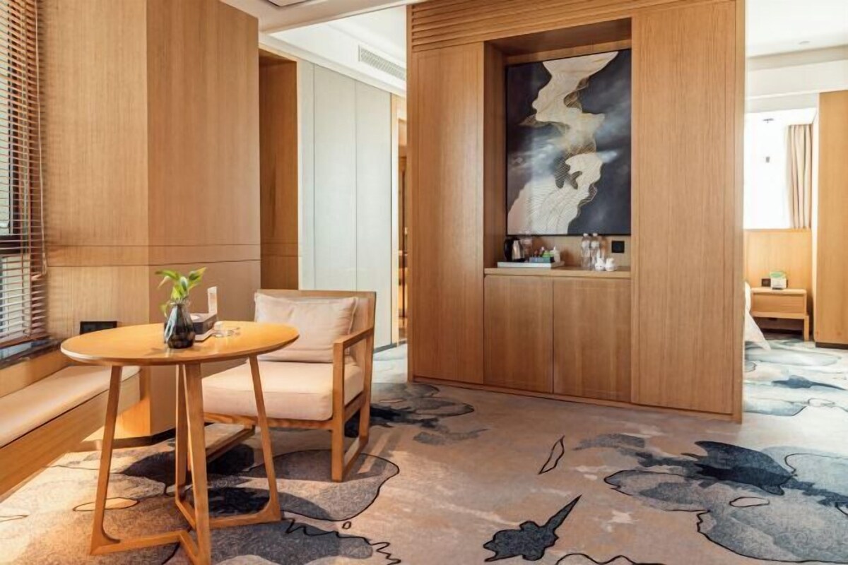 A modern hotel lobby with a wooden reception desk, a seating area with a sofa, and a decorative wall piece.