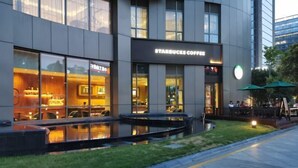 Una tienda Starbucks Coffee con grandes ventanales de vidrio, mesas al aire libre y una pequeña fuente en la fachada.