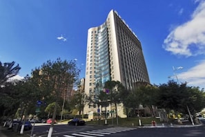 Un edificio alto de diseño moderno, rodeado de árboles y un paso de peatones.